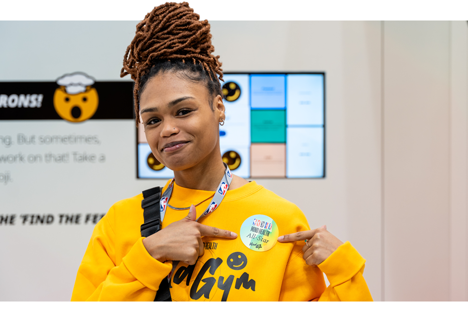 Photo of a young woman at an NBA Mind Health All-Star event, pointing to an NBA sticker on her sweatshirt